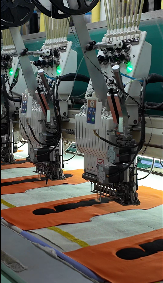 Close-up of embroidery machines stitching orange and black garment panels