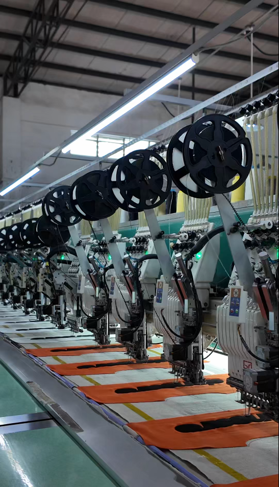 A line of embroidery heads working on orange garment panels in the HUAJUN factory